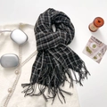 Classic black and white checkered knit scarf with tassels laid over a white tweed jacket - Black