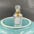 Macro shot of faceted crystal perfume bottle with a gold collar on a blue ceramic dish - White Crystal