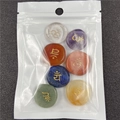 Dettaglio di sette pietre chakra con simboli dorati in un sacchetto trasparente - Set di 7 Pezzi