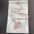 Dettaglio macro del pendolo in quarzo rosa esagonale con catena d'argento su sfondo scuro - Stile Pendolo / Rosa