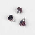 Three natural raw garnet pendants with silver-plated edging on a white textured background - Garnet