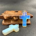 Translucent light blue crystal cross pendant with silver metal bail on wooden base - Opalite