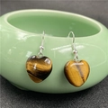 Detail of heart-shaped tiger eye stone earrings hanging on a green ceramic bowl rim - Tiger's Eye