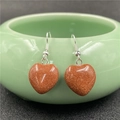 Detail of heart-shaped goldstone earrings hanging on a green ceramic bowl edge - Gold Sandstone