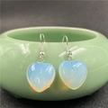 Close-up of heart-shaped light blue natural stone earrings hanging on a ceramic bowl edge - Opal