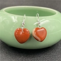 Macro shot of red heart-shaped natural stone earrings hanging on a green bowl edge - Rainbow Stone