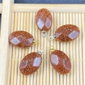 Macro shot of oval goldstone pendants with glittering sparkles on a natural bamboo tray - Gold Sandstone