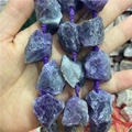 Gros plan de perles d'améthyste brute tenues à la main pour création de bijoux - Améthyste foncée