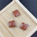 Detail of three clover-shaped red sandstone charms with silver rings on a bamboo tray - Gold Sandstone Pendant (Synthetic)
