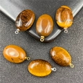 Close-up van zes ovale tijgeroogstenen hangers met gepolijste textuur en metalen oogjes - Tijgeroog Met Gouden Clip
