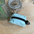 Bolsa de nailon verde menta con cremallera negra y mosquetón sobre superficie de madera - Verde Menta
