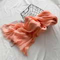 Écharpe en lin rose corail avec pompons dans un panier noir sur une literie blanche - Rose