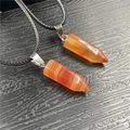 Detail of two hexagonal red agate crystal pendants with silver clasps on black wood grain - Red Agate