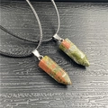 Close-up of hexagonal unakite crystal pendants on black cord over dark wood texture - Unakite