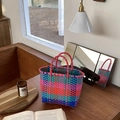 Detail of colorful checkerboard woven basket bag with round handles on a wooden table - Rose Red Patchwork