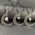 Close-up of hollow crescent moon pendant with light green gemstone on black background - Prehnite