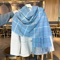 Sciarpa a quadri blu con nappe e accenti arancioni appesa a un cappotto grigio lana - Azzurro