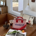 Detail der rot gestreiften Canvas-Tasche mit Smile-Stickerei auf einem Holztisch - Rot