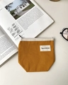 Close-up of mustard yellow canvas mini pouch with zipper on a minimalist book background - Orange