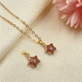 Elegante collar con colgante de estrella dorada y piedra arenisca roja sobre tela beige - Piedra de Oro Sintética