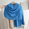 Solid blue cashmere-feel tassel scarf elegantly draped over a beige winter coat - No.10 Lake Blue