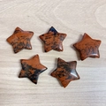 Five star-shaped red jasper stone carvings with black specks on wood surface - Mahogany Obsidian