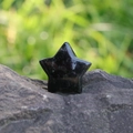 Polished obsidian star-shaped gemstone carving for home decor on a natural rock background - Obsidian