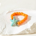 Detail of orange beaded ring with a light blue starfish charm on a stone background - Light Blue Sea Star Style (31026-ring-ora)