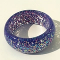 Macro detail of cobalt blue resin bangle featuring sparkling multicolored holographic flakes - Purple