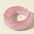 Close-up of pink resin bangle with sparkling glitter particles in bright lighting - Pink