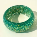 Detail view of wide green resin bangle with embedded colorful laser sequins and sparkles - Green