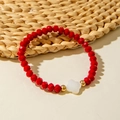 Detail shot of a red crystal beaded bracelet with white clover charm on a woven mat - Red