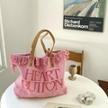 Rosa gewebte Tragetasche mit Fransen und besticktem Heart Button Text auf einem weißen Tisch - Rosa