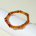 Detail of amber acrylic bamboo tube bracelet with gold metal spacer beads on white stand - Brown