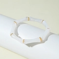 Dettaglio del bracciale elastico stile bambù bianco con sfere dorate su espositore - Trasparente