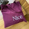 Nahaufnahme der burgunderroten Cord-Einkaufstasche mit weißem Nice-Stickmotiv und Druckknopf - Dunkelviolett
