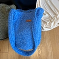 Blaue flauschige Plüschtasche mit Lederetikett auf einem Holzboden liegend - Hellblau