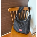 Sac hobo en toile noire à pois blancs avec étiquette rose posé sur une chaise - Style à Pois Noirs