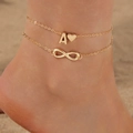 Detailed view of a layered gold anklet with A-letter, heart and infinity charms on a beach - Double Layer Letter A Heart & Infinity (30935-ank-1-G-EP)