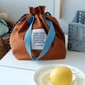 Detail van de bruine lunchtas met trekkoord, blauwe handvatten en wit geweven label - Bruin Kleurblok Bento Tas