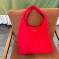 Grand sac cabas en nylon rouge vif avec texte Camellia blanc sur un fauteuil en cuir - Sac à bandoulière rouge avec imprimé lettres CAME