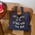 Dettaglio borsa tote in tela blu navy con testo bianco su una sedia in legno - Stile Stampato Blu Navy