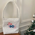 Dettaglio della borsa in tela trapuntata bianca con ricamo di cucciolo rosa su tavolo in legno - Borsa a tracolla cucciolo rosa a pois blu lato AB