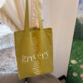 Close-up of olive green canvas tote bag with white grocery and herbal plant print - Green
