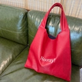 Large red leather tote bag with Hooray! text and wide strap on green sofa background - Red