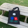 Borsa tote in tela nera minimalista con ricami floreali posata su una panca - Nero