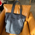 Dunkelblaue Denim-Tragetasche mit Vordertasche und stabilen Trägern auf Ledersofa - Dunkelblauer Denim