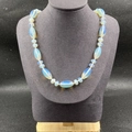 Detail einer Perlenkette mit blau-opalen Steinen auf einer grauen Schmuckbüste - Synthetischer Opal