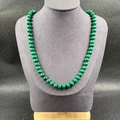 Green malachite wheel bead necklace with hand-knotted cord on display stand - Malachite
