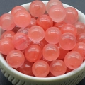 Polished 8mm translucent pink crystal round beads displayed in a white ceramic bowl - Watermelon Red (Synthetic)